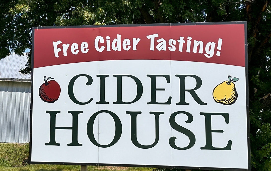 Sign for Cider House offering free cider tasting in front of a building with trees in the background.